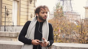 Type de mulâtre appréciant le smartphone et les écouteurs avec Tour Eiffel à l'arrière-plan dans le mouvement lent clips vidéos Type de mulâtre appréciant le smartphone et les écouteurs avec Tour Eiffel à l'arrière-plan dans le mouvement lent clips vidéos