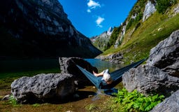 Type refroidissant dans un hamac entre deux pierres à un lac de montagne enjoing la vue image stock Type refroidissant dans un hamac entre deux pierres à un lac de montagne enjoing la vue image stock
