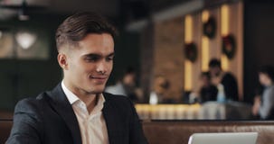 Té de consumición sonriente y usar del hombre de negocios la sentada del ordenador portátil en la tabla del café metrajes Té de consumición sonriente y usar del hombre de negocios la sentada del ordenador portátil en la tabla del café metrajes