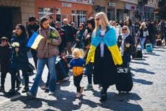 A Ukrainian refugee wrapped in a Ukrainian flag walks with a child.