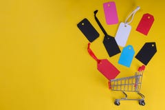 Um carrinho de compras com etiquetas e os preços multi-coloridos em um fundo amarelo brilhante de um conceito preto de sexta-feir fotos de stock Um carrinho de compras com etiquetas e os preços multi-coloridos em um fundo amarelo brilhante de um conceito preto de sexta-feir fotos de stock