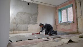 Um construtor que trabalhe em lugares de moradia a telha no assoalho e verifique a inclinação e a regularidade do assoalho com o Um construtor que trabalhe em lugares de moradia a telha no assoalho e verifique a inclinação e a regularidade do assoalho com o