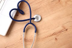 Um estetoscópio médico perto de um portátil em uma tabela de madeira, no branco imagem de stock Um estetoscópio médico perto de um portátil em uma tabela de madeira, no branco imagem de stock
