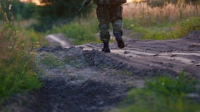 Um homem armado em uniformes da camuflagem anda ao longo de uma estrada de terra no por do sol Vista traseira vídeos de arquivo Um homem armado em uniformes da camuflagem anda ao longo de uma estrada de terra no por do sol Vista traseira vídeos de arquivo