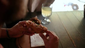um homem com uma barba e um tampão guarda um sanduíche em suas mãos, e morde-o então ao sentar-se em um café Vista de acima 4K 4k video estoque um homem com uma barba e um tampão guarda um sanduíche em suas mãos, e morde-o então ao sentar-se em um café Vista de acima 4K 4k video estoque