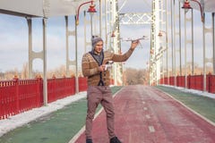 Um homem considerável novo da aparência europeia lança um zangão no fundo de um céu azul em uma ponte no inverno foto de stock royalty free Um homem considerável novo da aparência europeia lança um zangão no fundo de um céu azul em uma ponte no inverno foto de stock royalty free