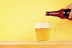 Um homem derrama a cerveja em uma caneca de uma garrafa em um fundo amarelo em uma tabela de madeira Copie o espaço fotografia de stock Um homem derrama a cerveja em uma caneca de uma garrafa em um fundo amarelo em uma tabela de madeira Copie o espaço fotografia de stock