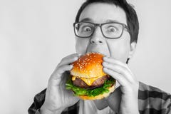 Um indivíduo novo com os vidros que guardam um hamburguer fresco Um estudante muito com fome come o fast food O conceito da gluto imagens de stock royalty free Um indivíduo novo com os vidros que guardam um hamburguer fresco Um estudante muito com fome come o fast food O conceito da gluto imagens de stock royalty free