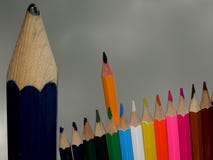 Um lápis desalinhado grande, estando ao lado de um grupo pequeno Sharp esperto de lápis coloridos imagens de stock Um lápis desalinhado grande, estando ao lado de um grupo pequeno Sharp esperto de lápis coloridos imagens de stock