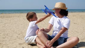 Um menino de sorriso pequeno joga com um plano que descreve o voo O bebê e a mãe são descansar, sentando-se na costa arenosa na vídeos de arquivo Um menino de sorriso pequeno joga com um plano que descreve o voo O bebê e a mãe são descansar, sentando-se na costa arenosa na vídeos de arquivo