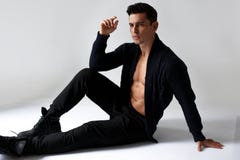Um modelo 'sexy', muscular do homem novo, no torso despido no preto, sentando-se no estúdio, no fundo branco fotos de stock Um modelo 'sexy', muscular do homem novo, no torso despido no preto, sentando-se no estúdio, no fundo branco fotos de stock