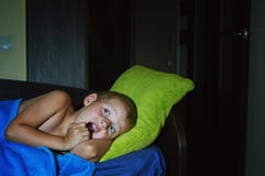 Um rapaz pequeno assustado receoso na cama na noite, infância teme foto de stock Um rapaz pequeno assustado receoso na cama na noite, infância teme foto de stock