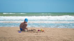 Um rapaz pequeno está jogando na areia no mar, os pés e os dedos pequenos, um fundo da areia amarela do mar e água azul filme Um rapaz pequeno está jogando na areia no mar, os pés e os dedos pequenos, um fundo da areia amarela do mar e água azul filme
