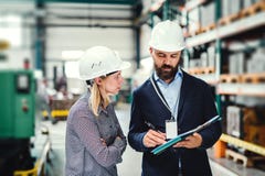 Um retrato de um coordenador industrial do homem e da mulher com prancheta em uma fábrica, trabalhando imagem de stock Um retrato de um coordenador industrial do homem e da mulher com prancheta em uma fábrica, trabalhando imagem de stock
