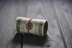 Um rolo grosso de cem cédulas do dólar amarrou um elástico vermelho encontra-se na tabela de madeira cinzenta fotos de stock Um rolo grosso de cem cédulas do dólar amarrou um elástico vermelho encontra-se na tabela de madeira cinzenta fotos de stock
