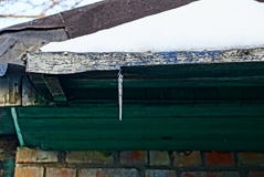 Um sincelo pequeno em um telhado verde sob a neve fotografia de stock Um sincelo pequeno em um telhado verde sob a neve fotografia de stock