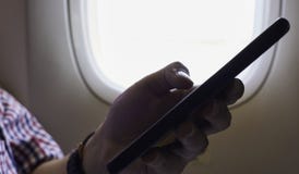 Um telefone celular da terra arrendada da mão dentro do avião perto da janela foto de stock Um telefone celular da terra arrendada da mão dentro do avião perto da janela foto de stock