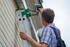 Um técnico masculino está fazendo o trabalho de manutenção inspecionando e limpando uma segurança exterior imagem de stock Um técnico masculino está fazendo o trabalho de manutenção inspecionando e limpando uma segurança exterior imagem de stock