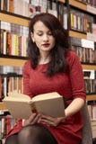 Uma jovem mulher que lê um livro, sentando-se em uma livraria imagens de stock Uma jovem mulher que lê um livro, sentando-se em uma livraria imagens de stock