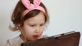 Uma menina bonito manuseia uma lista de músicas na tabuleta, escolhe-a e escuta-à música nos fones de ouvido Criança engraçada co vídeos de arquivo Uma menina bonito manuseia uma lista de músicas na tabuleta, escolhe-a e escuta-à música nos fones de ouvido Criança engraçada co vídeos de arquivo