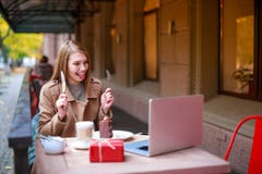 Uma menina em um café exterior com um portátil que fala a alguém com uma chamada video, guardando a cutelaria em suas mãos fotografia de stock Uma menina em um café exterior com um portátil que fala a alguém com uma chamada video, guardando a cutelaria em suas mãos fotografia de stock