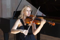Uma menina loura bonita no vestido preto com bordos vermelhos joga um violino foto de stock royalty free Uma menina loura bonita no vestido preto com bordos vermelhos joga um violino foto de stock royalty free