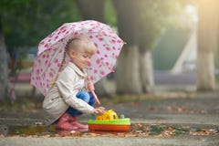 Uma menina que joga na poça com o barco após a chuva imagem de stock Uma menina que joga na poça com o barco após a chuva imagem de stock