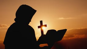 Uma monge em uma capa com um crucifixo em suas m?os est? contra o contexto de um c?u dram?tico no por do sol imagens de stock royalty free Uma monge em uma capa com um crucifixo em suas m?os est? contra o contexto de um c?u dram?tico no por do sol imagens de stock royalty free