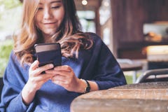 Uma mulher asiática bonita com cara do smiley usando e olhando um telefone esperto preto imagens de stock Uma mulher asiática bonita com cara do smiley usando e olhando um telefone esperto preto imagens de stock