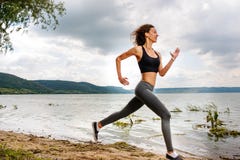 Uma mulher desportiva bonita que corre na costa de um lago nos esportes fotografia de stock Uma mulher desportiva bonita que corre na costa de um lago nos esportes fotografia de stock