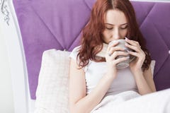 Uma mulher moreno nova atrativa senta-se em sua cama com uma caneca e os comprimidos Frios e tratamento da casa fotografia de stock Uma mulher moreno nova atrativa senta-se em sua cama com uma caneca e os comprimidos Frios e tratamento da casa fotografia de stock