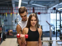 Uma mulher que faz exercícios com pesos em um fundo do gym Um instrutor pessoal que ajuda um cliente em um clube de aptidão foto de stock Uma mulher que faz exercícios com pesos em um fundo do gym Um instrutor pessoal que ajuda um cliente em um clube de aptidão foto de stock