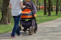 Uma mãe nova está andando com um carrinho de criança de bebê em um parque do verão em um dia ensolarado imagem de stock Uma mãe nova está andando com um carrinho de criança de bebê em um parque do verão em um dia ensolarado imagem de stock