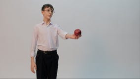 Un adolescent en verres, utilisant une chemise blanche et un pantalon noir, tient une pomme dans des ses mains et l'étire en avan image stock Un adolescent en verres, utilisant une chemise blanche et un pantalon noir, tient une pomme dans des ses mains et l'étire en avan image stock