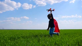 Un bambino in un mantello rosso e nei funzionamenti della maschera, tenenti un aereo in sua mano, rappresentante il volo archivi video Un bambino in un mantello rosso e nei funzionamenti della maschera, tenenti un aereo in sua mano, rappresentante il volo archivi video