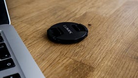 Un capuchon d'objectif de lumix de panasonic à côté d'un macbook photo libre de droits Un capuchon d'objectif de lumix de panasonic à côté d'un macbook photo libre de droits