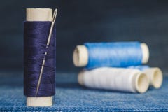 Un carrete de hilos azules con una aguja de costura en el fondo de los carretes de hilos azules y blancos en una tela del dril de fotografía de archivo libre de regalías Un carrete de hilos azules con una aguja de costura en el fondo de los carretes de hilos azules y blancos en una tela del dril de fotografía de archivo libre de regalías