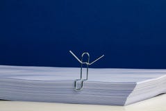Un carácter del clip de papel que lleva a cabo las manos para arriba en la resma de papel fotografía de archivo Un carácter del clip de papel que lleva a cabo las manos para arriba en la resma de papel fotografía de archivo