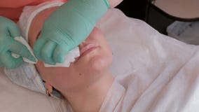 Un cosmetologist-thérapeute professionnel essuie les restes d'un gel cosmétique transparent d'un visage femelle Fille avec clips vidéos Un cosmetologist-thérapeute professionnel essuie les restes d'un gel cosmétique transparent d'un visage femelle Fille avec clips vidéos