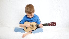 Un enfant heureux s'assied sur un sofa blanc et joue la guitare pour des enfants clips vidéos Un enfant heureux s'assied sur un sofa blanc et joue la guitare pour des enfants clips vidéos