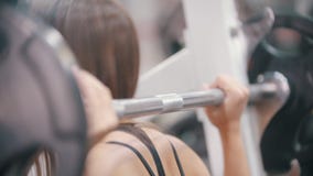 Un entrenamiento juguetón de la mujer en el gimnasio - consigue bajo pesa de gimnasia y la pone en sus hombros almacen de metraje de vídeo Un entrenamiento juguetón de la mujer en el gimnasio - consigue bajo pesa de gimnasia y la pone en sus hombros almacen de metraje de vídeo