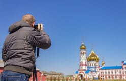 Un fotografo prende le immagini della chiesa sulla macchina fotografica con un treppiede fotografia stock Un fotografo prende le immagini della chiesa sulla macchina fotografica con un treppiede fotografia stock
