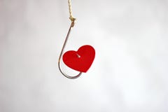 Un gancio di pesca del metallo che appende su una corda ha perforato il cuore rosso del cartone immagine stock Un gancio di pesca del metallo che appende su una corda ha perforato il cuore rosso del cartone immagine stock