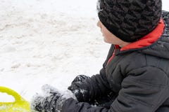 Un garçon de sept années se reposant sur la neige et un traîneau en plastique vert de soucoupe se trouvant près de lui Concept de images stock Un garçon de sept années se reposant sur la neige et un traîneau en plastique vert de soucoupe se trouvant près de lui Concept de images stock