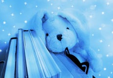 Un giocattolo della peluche del coniglio riposa la sua testa su una fila dei libri Bokeh ed effetto tonificati e molli blu della immagini stock libere da diritti Un giocattolo della peluche del coniglio riposa la sua testa su una fila dei libri Bokeh ed effetto tonificati e molli blu della immagini stock libere da diritti