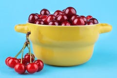 Un groupe de cerises mûres et fraîches avec une cerise dans une cuvette jaune sur un fond lumineux de papier bleu images libres de droits Un groupe de cerises mûres et fraîches avec une cerise dans une cuvette jaune sur un fond lumineux de papier bleu images libres de droits