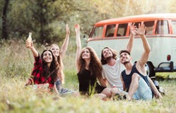 Un groupe de jeunes amis avec des boissons se reposant sur l'herbe sur une promenade en voiture par la campagne image stock Un groupe de jeunes amis avec des boissons se reposant sur l'herbe sur une promenade en voiture par la campagne image stock