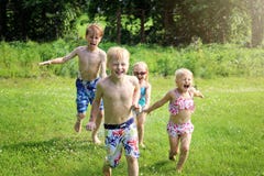 Un groupe de petits enfants heureux sourit pendant qu'ils fonctionnent par l'extérieur d'arroseuse un jour d'été image stock Un groupe de petits enfants heureux sourit pendant qu'ils fonctionnent par l'extérieur d'arroseuse un jour d'été image stock