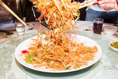 Un grupo de personas que mezcla y que lanza el plato de Yee Sang con tajada se pega Yee Sang es una delicadeza popular tomada dur Un grupo de personas que mezcla y que lanza el plato de Yee Sang con tajada se pega Yee Sang es una delicadeza popular tomada dur