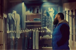 Un hombre barbudo en miradas del sporstwear a la ventana de la tienda con ropa del negocio foto de archivo libre de regalías Un hombre barbudo en miradas del sporstwear a la ventana de la tienda con ropa del negocio foto de archivo libre de regalías